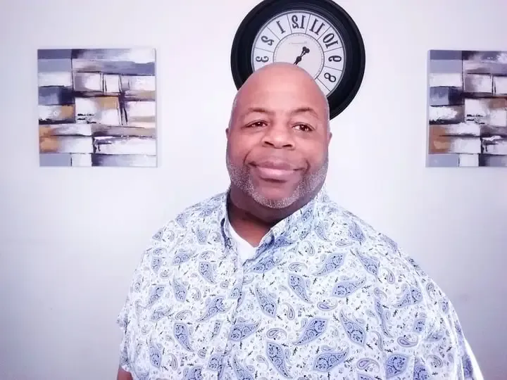 Apostle Daryl Johnson in a blue paisley shirt in front of the studio wall clock